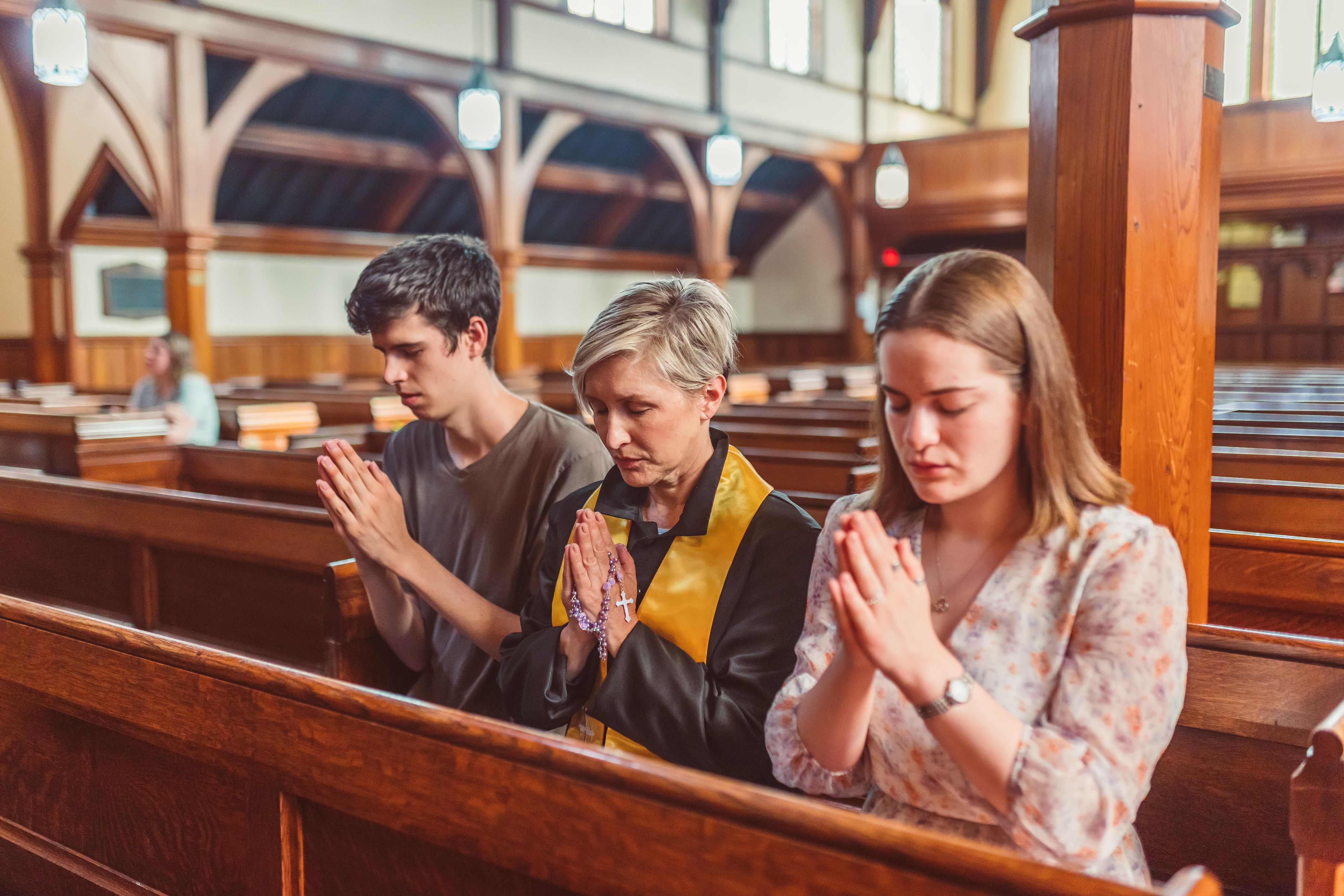 Three people praying in a church pew